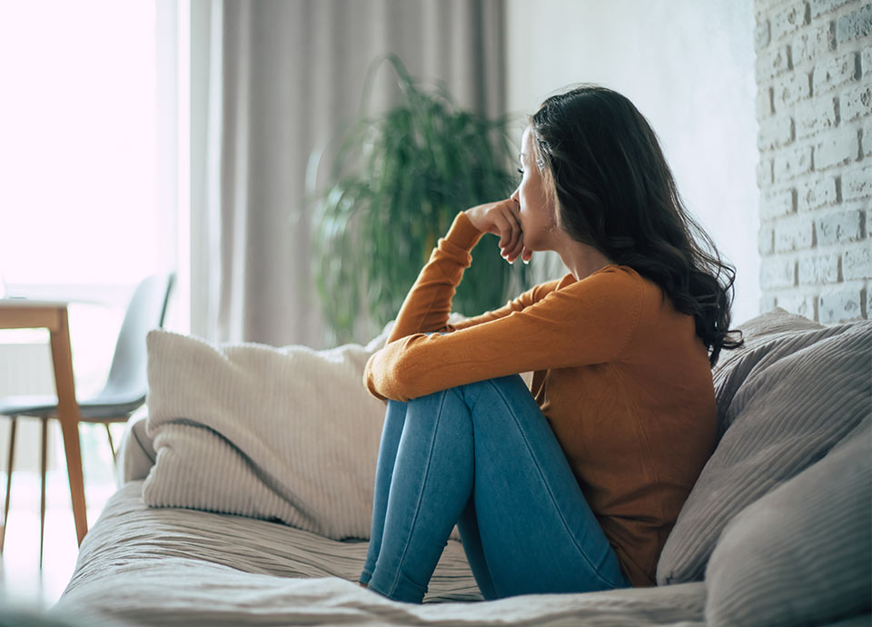 Eine Frau sitzt verzewifelt auf dem Sofa, sie ist länger krank und überlegt nun wie es finanziell weitergeht - GT Cap unterstützt mit dem Krankentagegeld